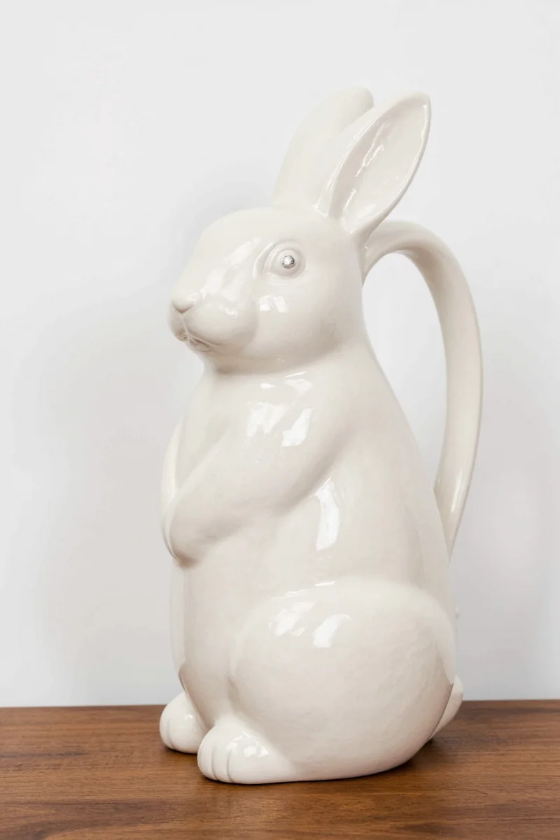 Close-up of a fluffy bunny lounging near a beautifully decorated kitchen counter with a bunny rabbit pitcher as the centerpiece.
