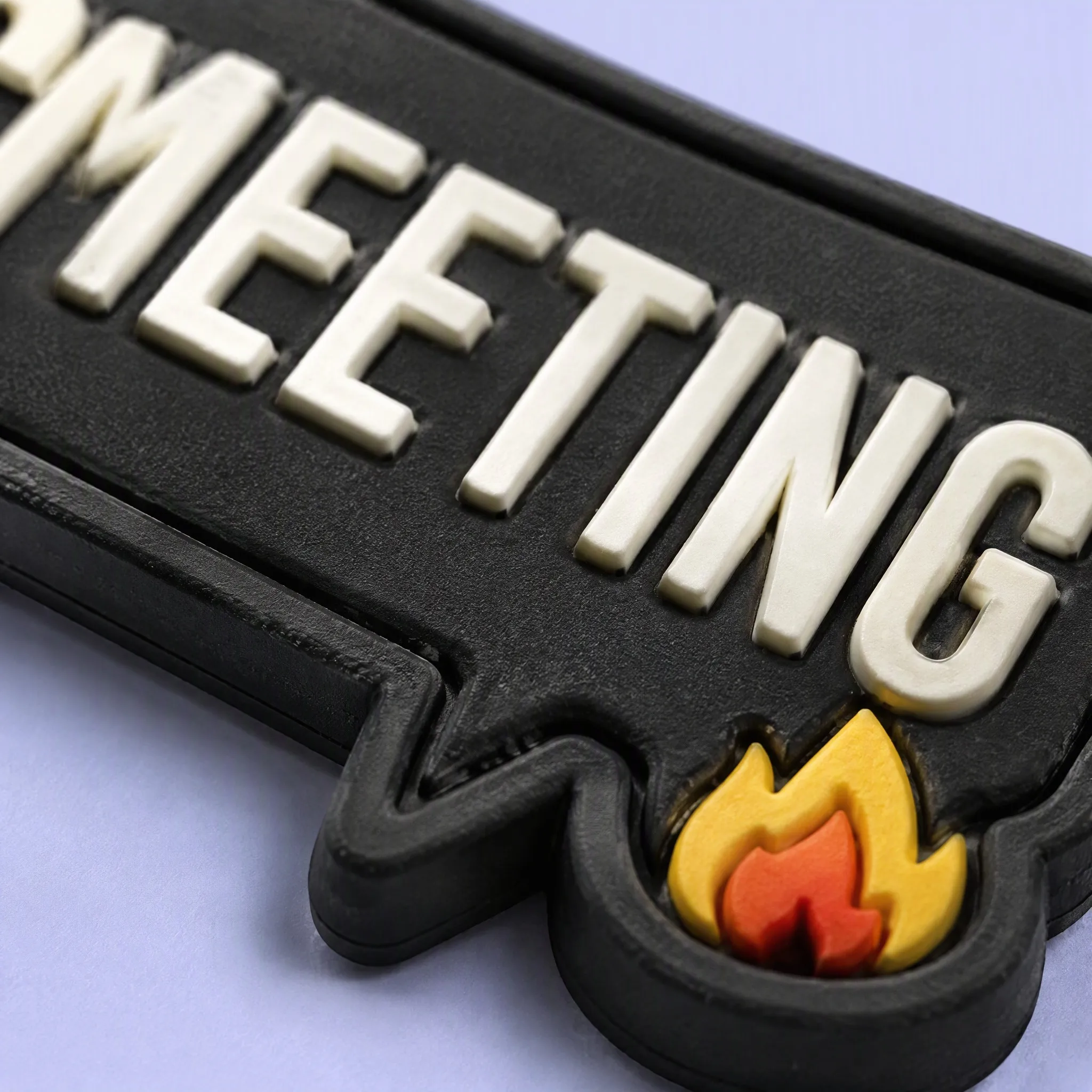 Super Macro Close-Up of 3D Embossed White Letters MEETING and Flame Icon on Black PVC Speech Bubble