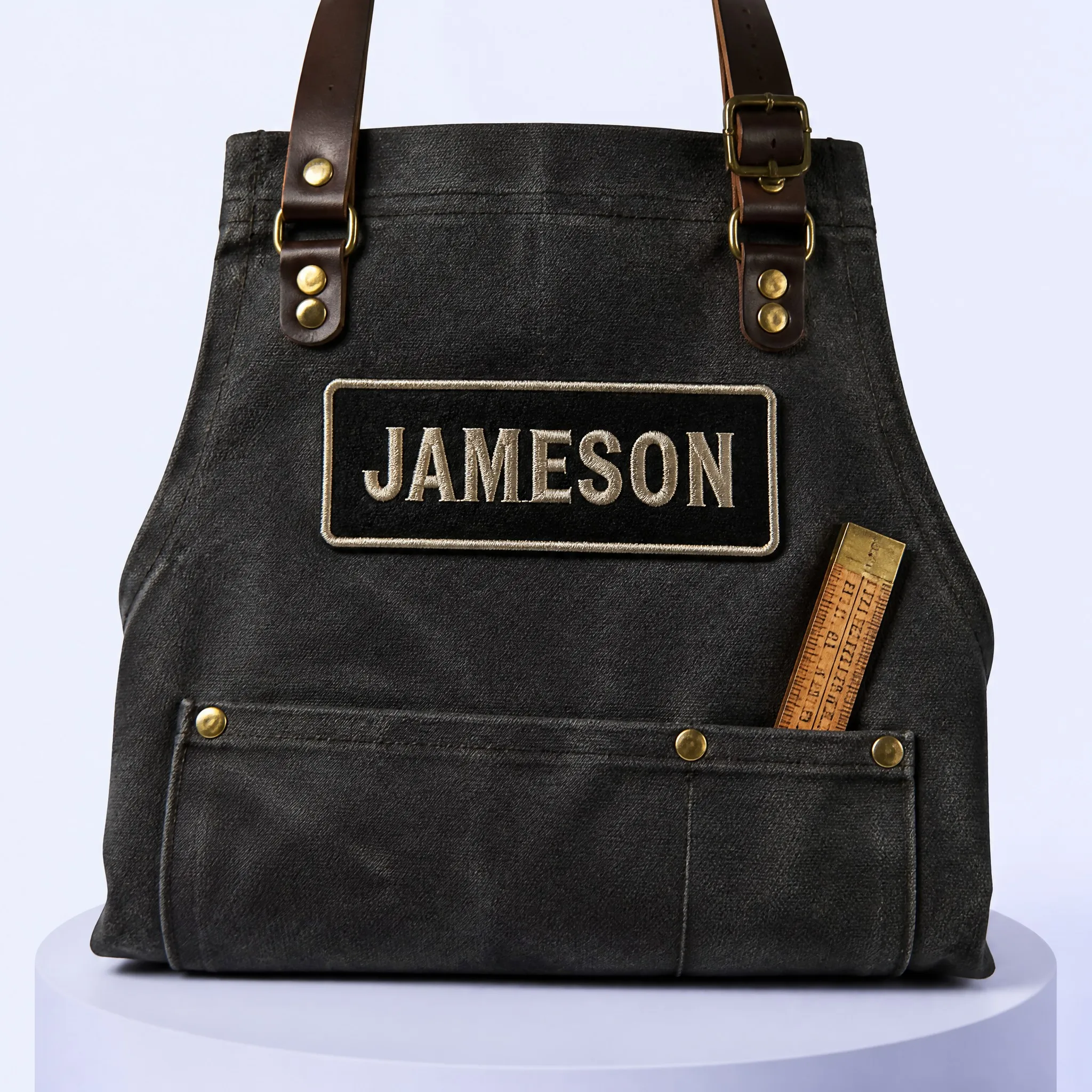 JAMESON Bold All-Caps Name Patch Stitched onto Dark Waxed Canvas Workshop Apron with Leather Straps and Brass Rivets